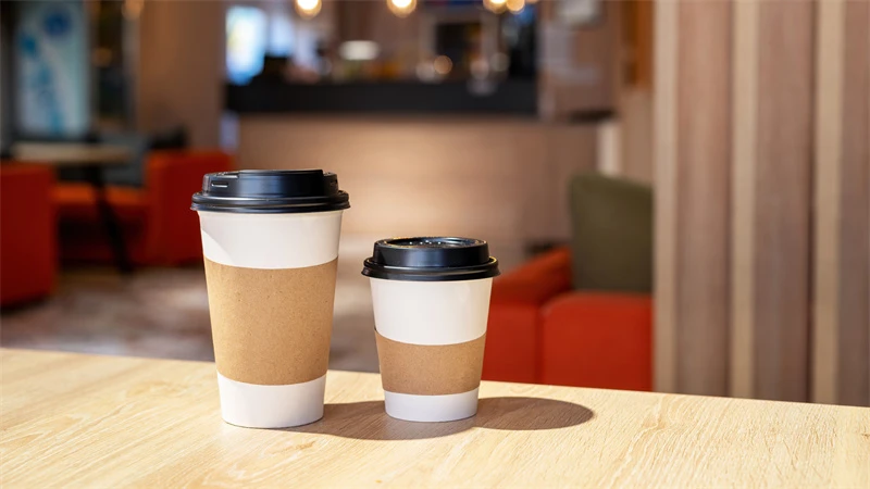Big Reveal: Where Do Cafes Buy Paper Coffee Cups From? blog cover: there are two different size paper coffee cups stand on the wooden desk